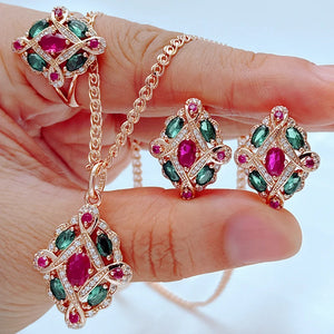 Rose gold jewelry set featuring ruby red and emerald green crystals with a matching pendant necklace, earrings, and ring in a vintage-inspired design.