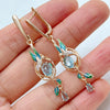 Rose gold floral drop earrings with aquamarine blue crystals, green enamel leaves, and sparkling accents.