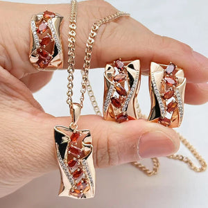 Rose gold red garnet jewelry set with pendant necklace, matching earrings, and ring featuring sparkling gemstone accents.